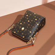 Crossbody Phone Bag by Foxer in brown PVC/microfiber with adjustable strap on a brown background.