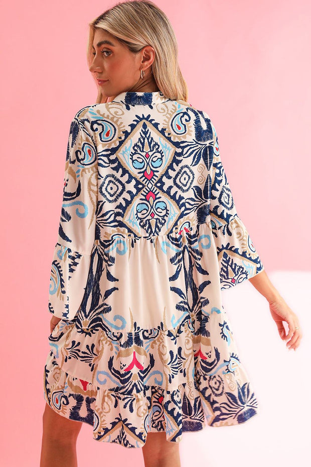 White Boho Print Mini Dress with blue and pink ethnic patterns on a model, featuring a playful ruffled hem.