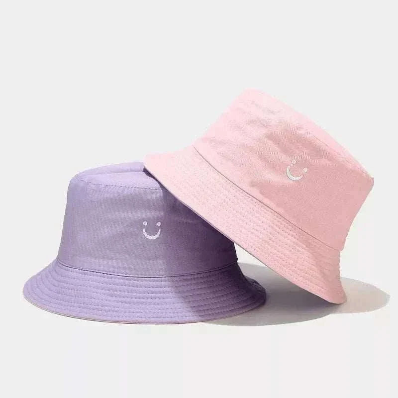 Women’s Smiley Face Bucket Hat in pink and lavender, with stitched smiley faces and classic brimmed cotton design