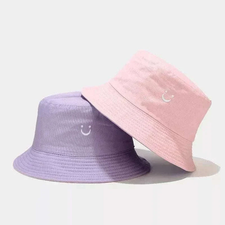 Women’s Smiley Face Bucket Hat in pink and lavender, with stitched smiley faces and classic brimmed cotton design