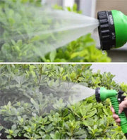 Flexible garden hose spraying water on green plants.