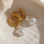 Elegant gold and pearl water drop earrings on a marble surface.