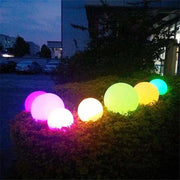 Glowing colorful Waterproof Garden LED Lights Ball on outdoor bush at night.