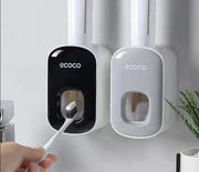 Automatic toothpaste dispenser with black and white wall-mounted units, featuring hands-free operation and integrated toothbrush holder.