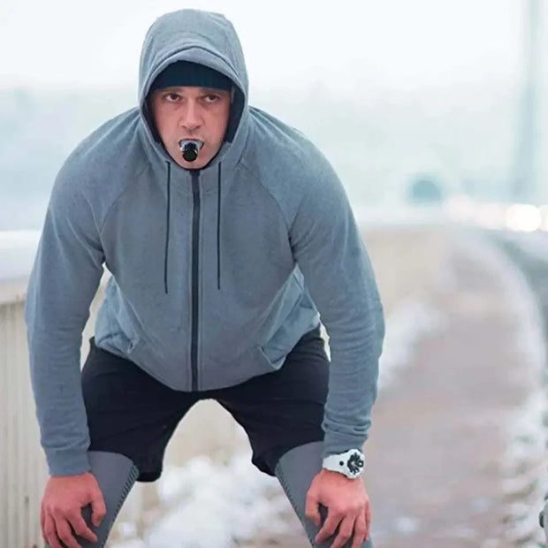 Man using Lung Fitness Trainer outdoors in cold weather, wearing a grey hoodie.