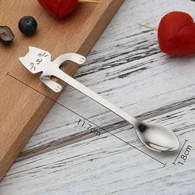 Stainless steel cat teaspoon with cute design on wooden surface.