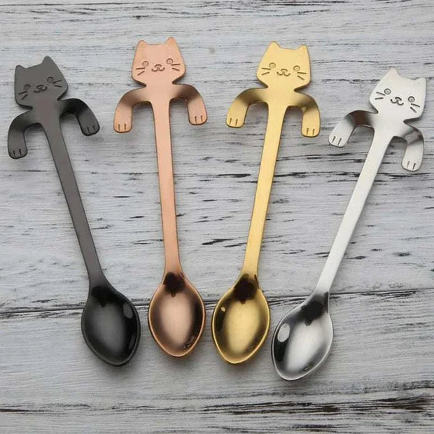 Adorable stainless steel cat-shaped teaspoons in various colors on a wooden surface.