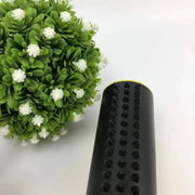 Pet hair remover brush with black sturdy bristles next to green artificial plant.