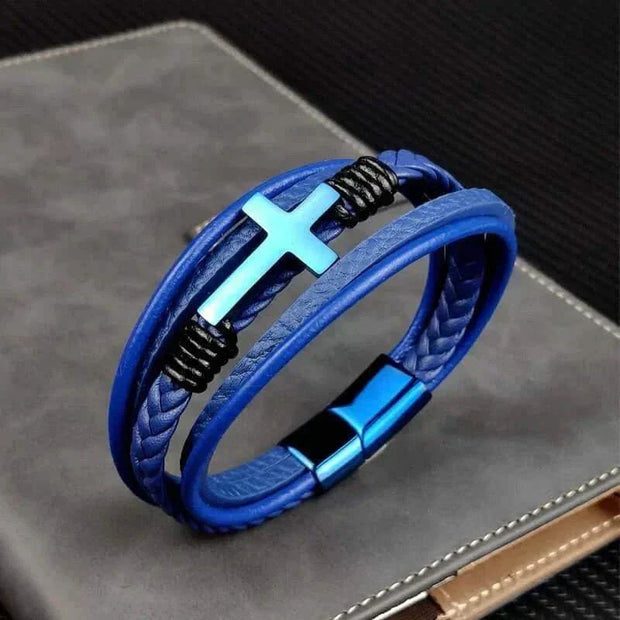Mens Chakra Bracelet with blue leather and cross charm on a textured surface.